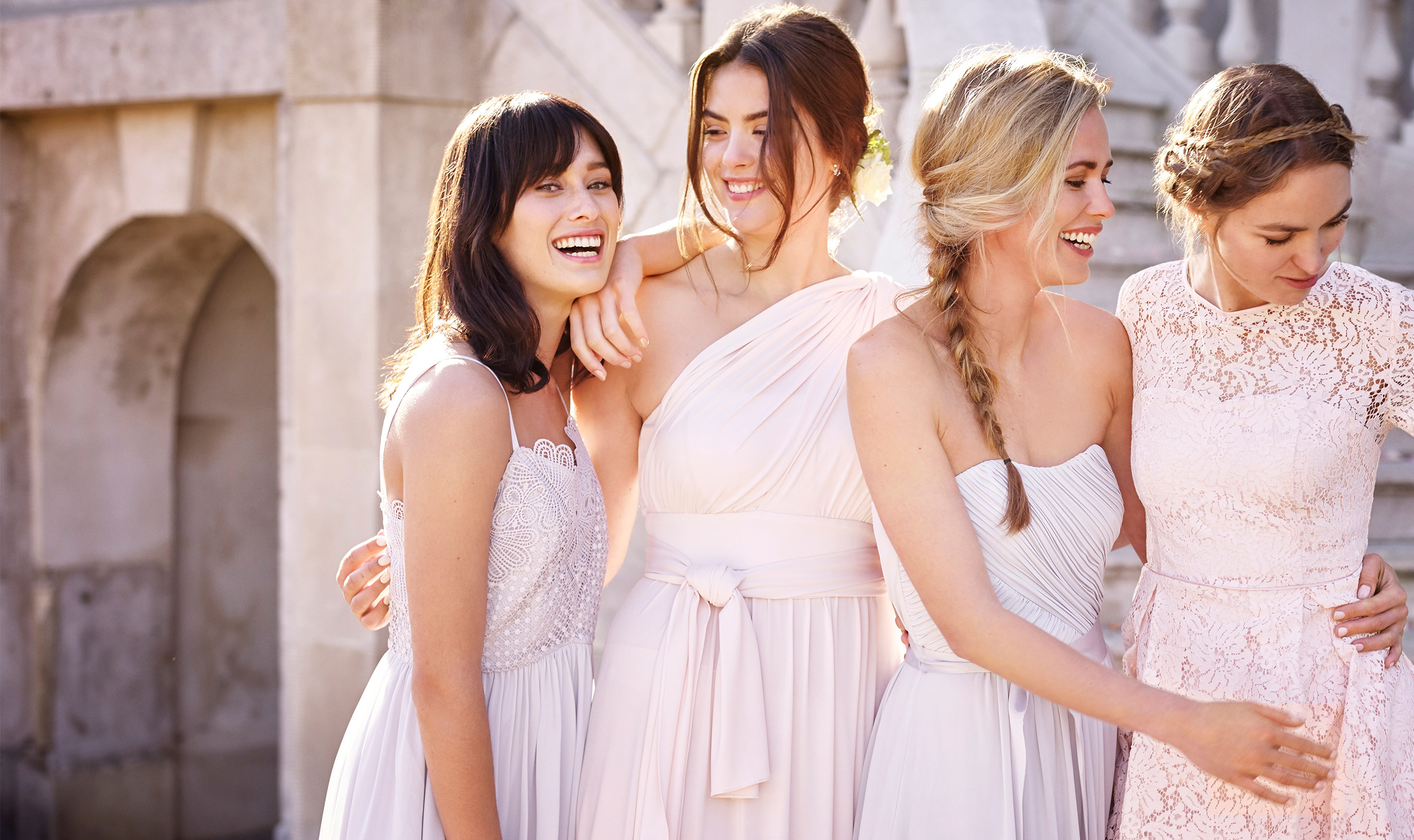 Four bridesmaids in pink and lilac-grey dresses by stone staircase